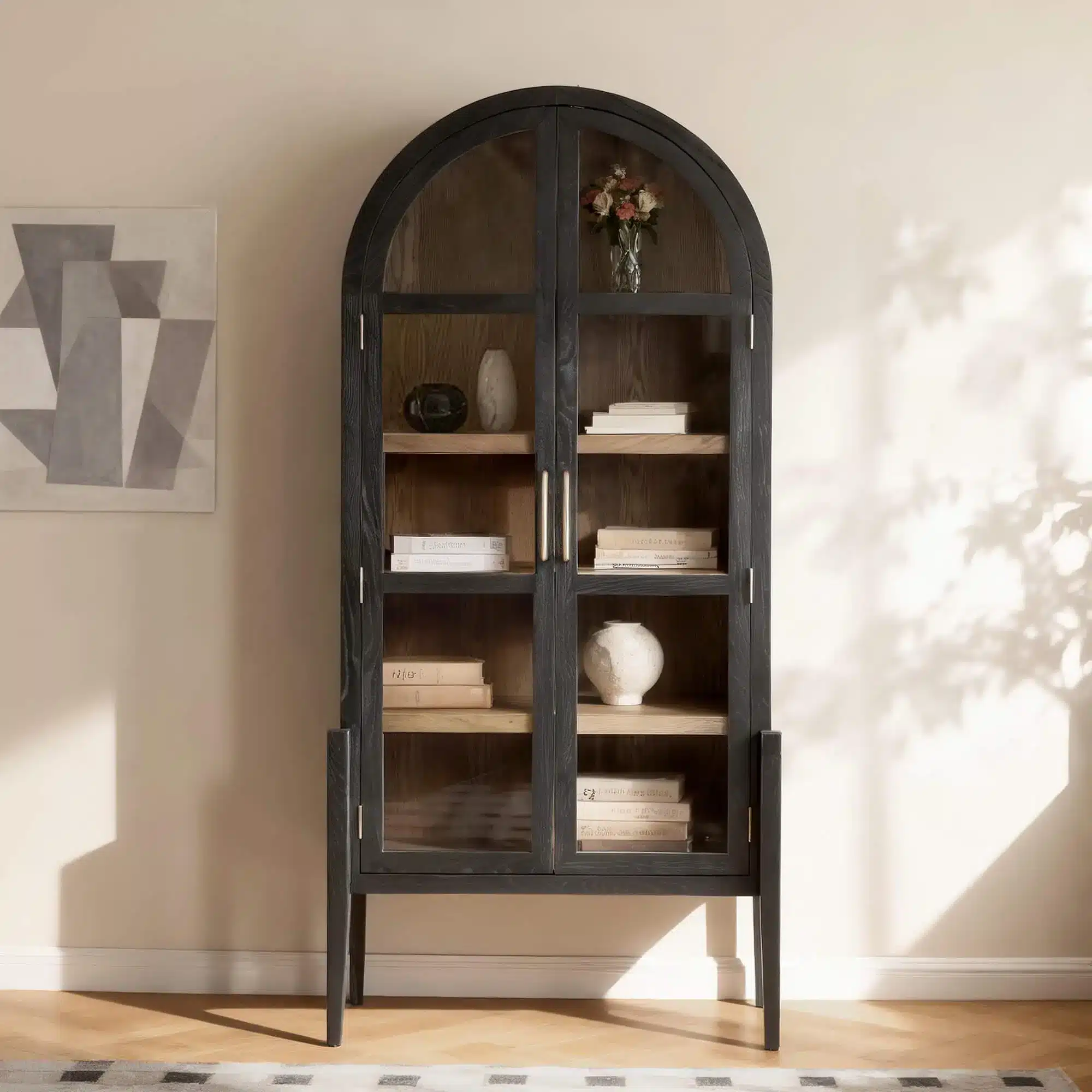Black wooden display cabinet with glass doors and shelves, in sunlit room with abstract wall art