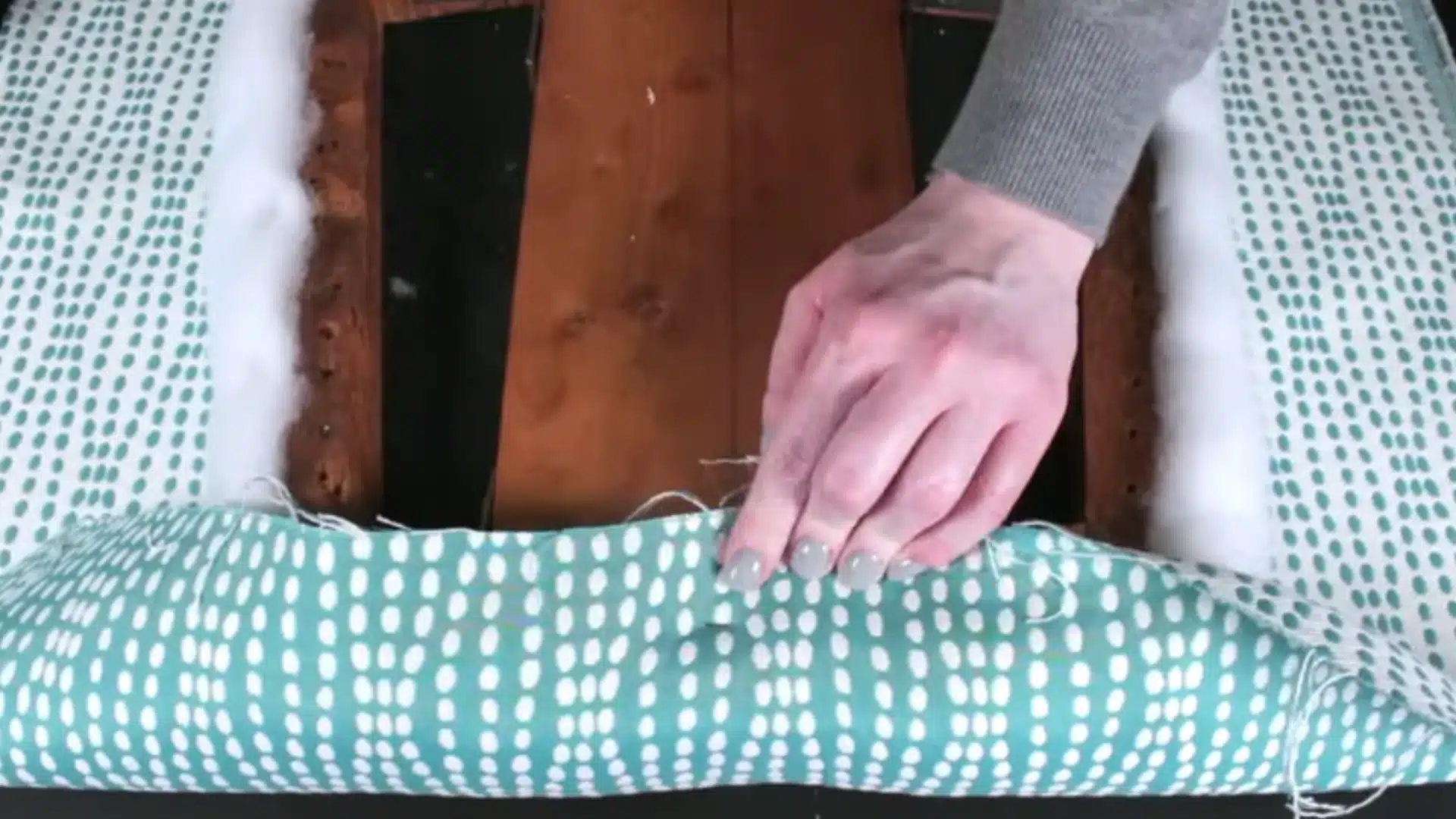 teal patterned upholstery fabric being pulled and secured around the padded wooden chair seat frame