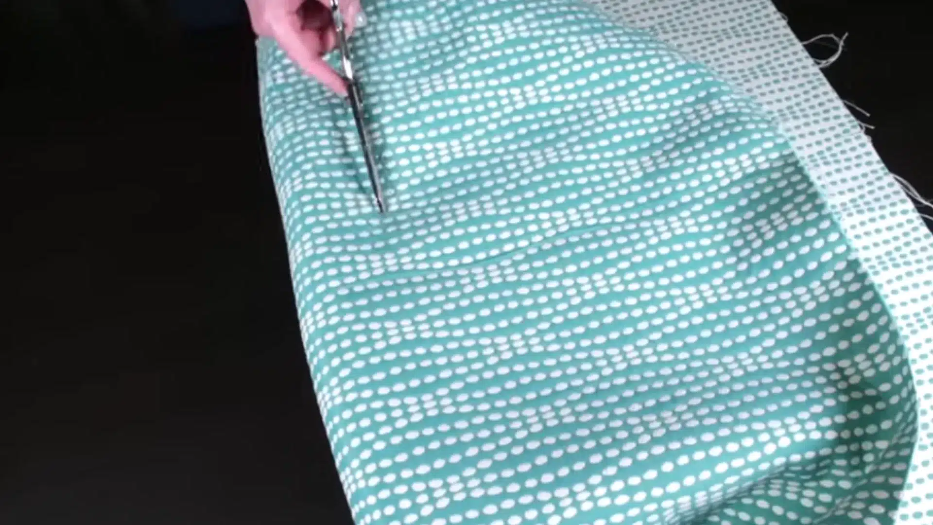 teal patterned upholstery fabric being trimmed with scissors to fit around the padded chair cushion