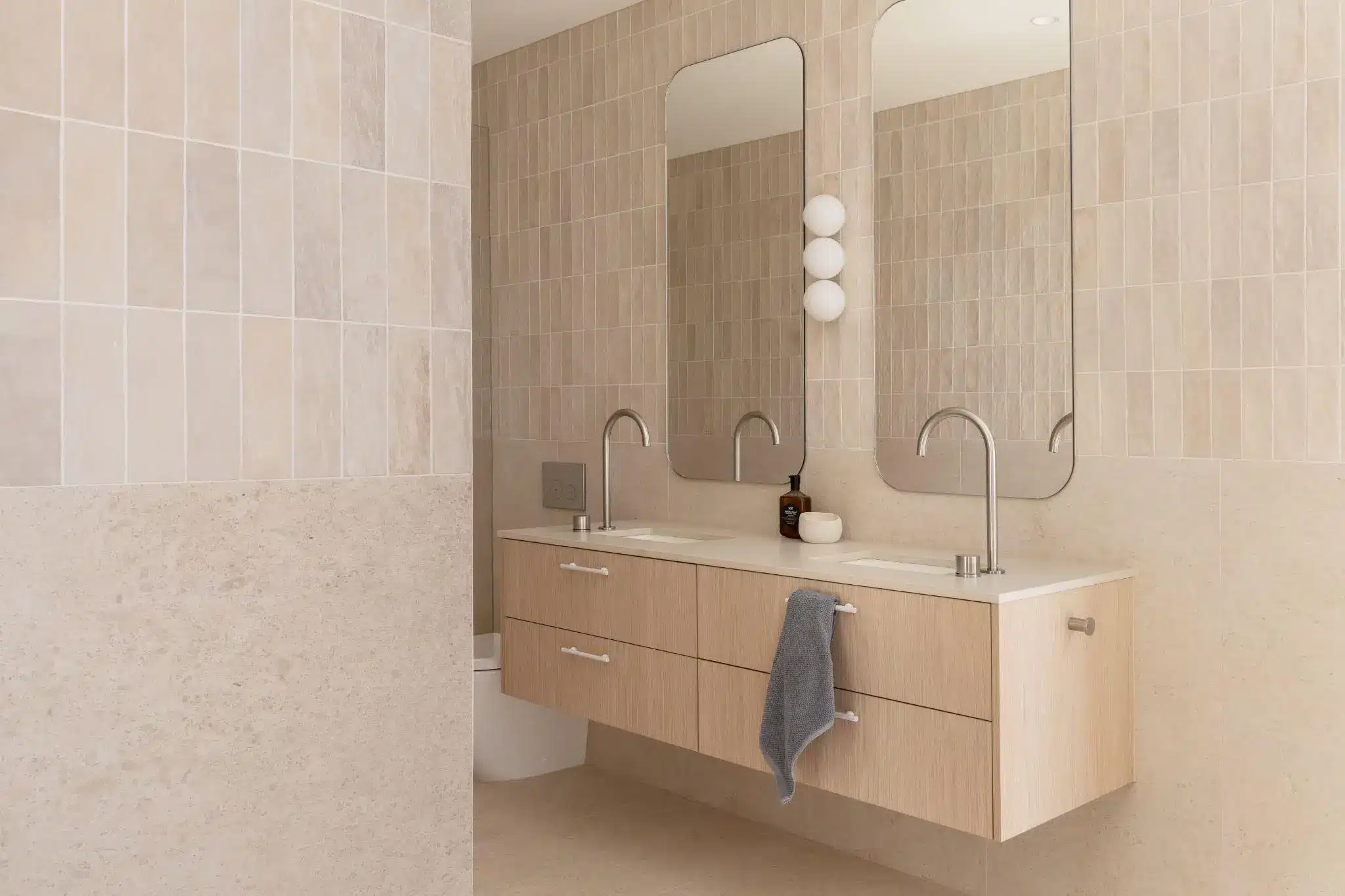 Modern bathroom with double vanity, large mirrors, and beige tiled walls