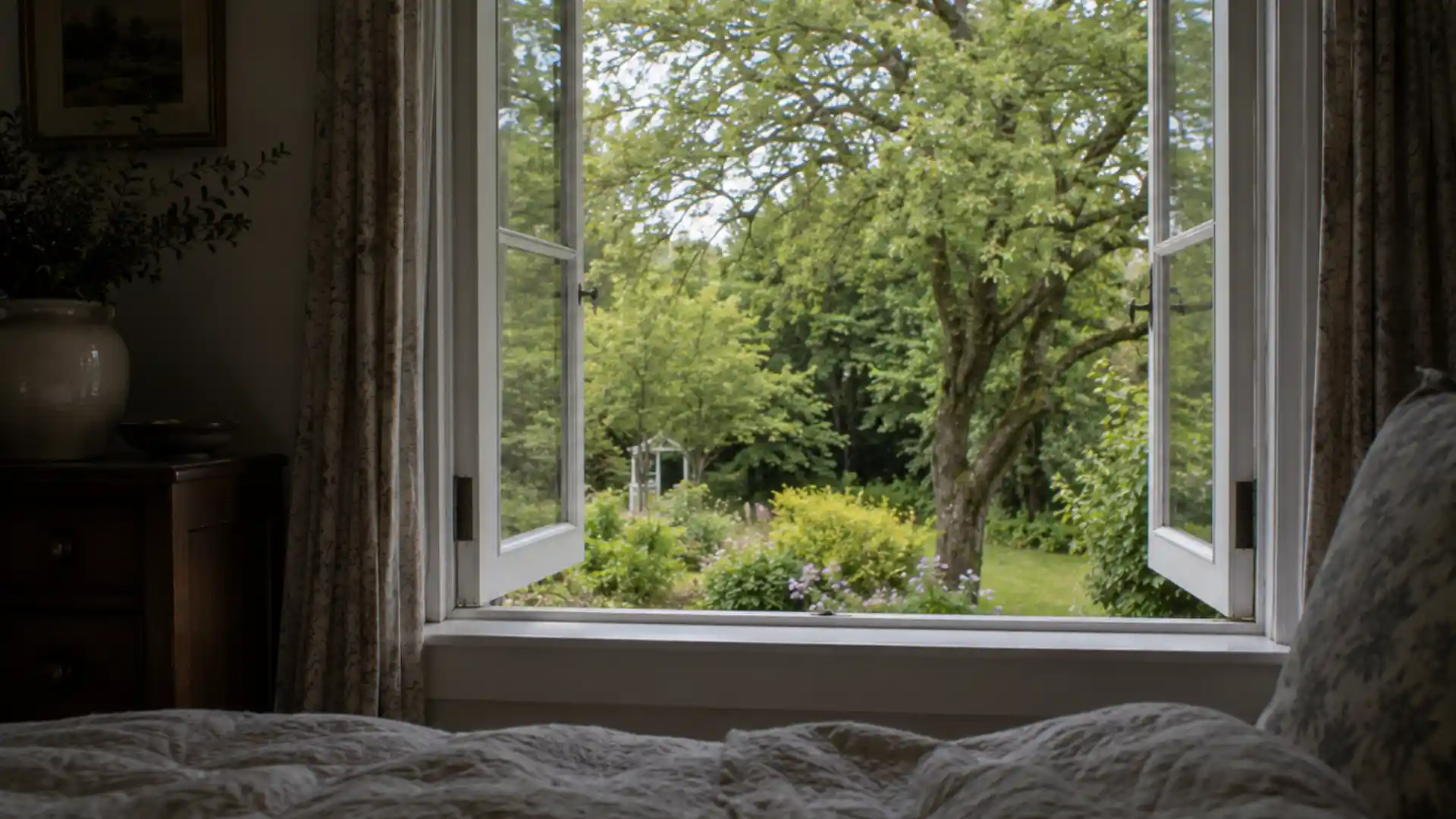 view from bed through an open window overlooking a green garden