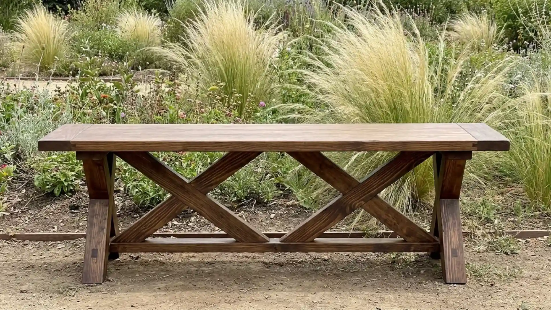 wooden bench with crossed x shaped legs standing among tall ornamental grasses