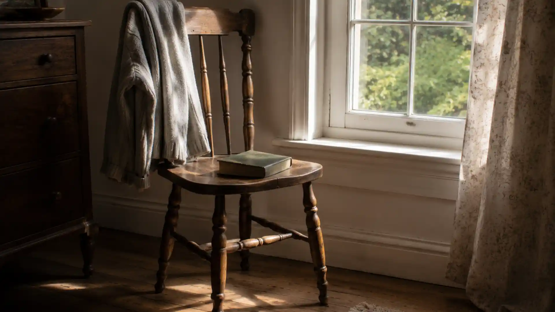 wooden chair by a window with a folded sweater and open book