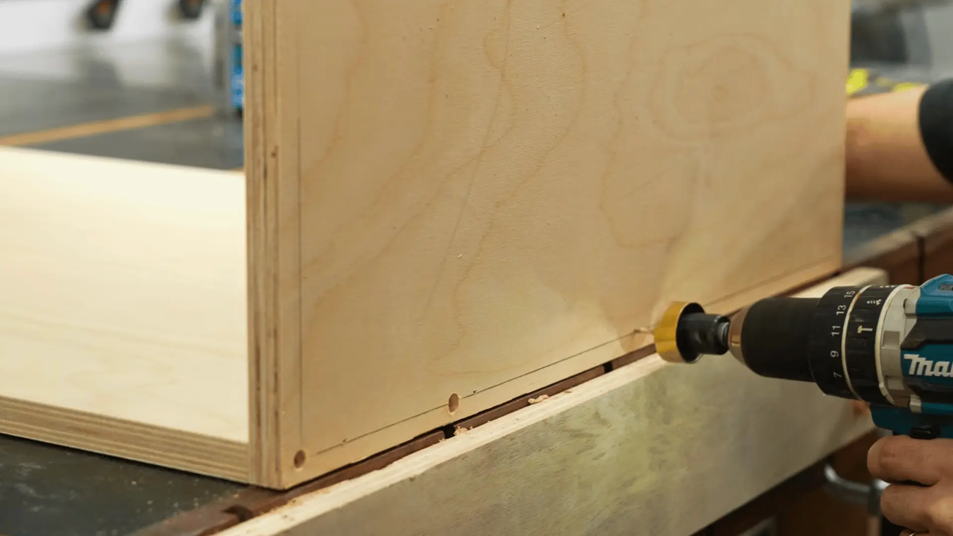 woodworker driving a screw into a plywood cabinet side panel with a drill during box assembly
