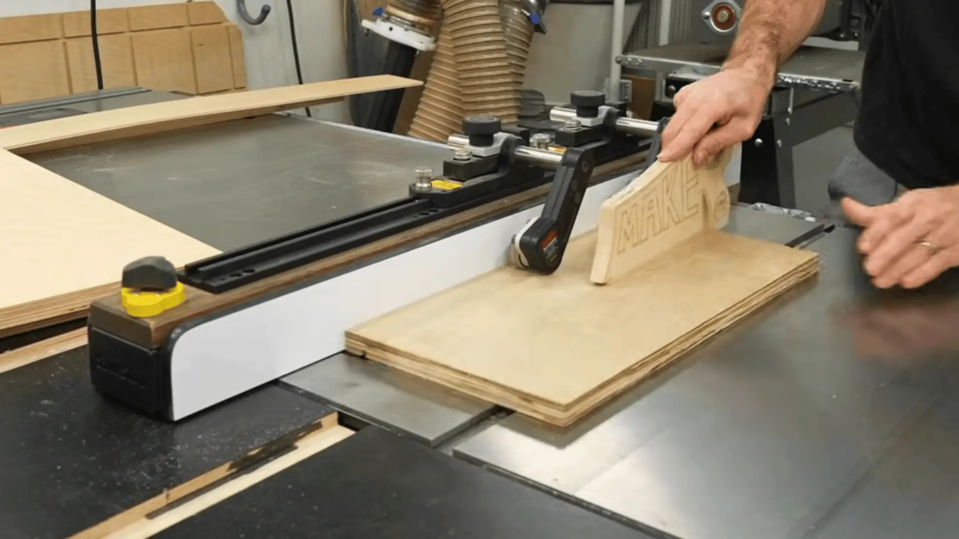 woodworker feeding a plywood panel through a table saw using a wooden crosscut sled clamped to the fence