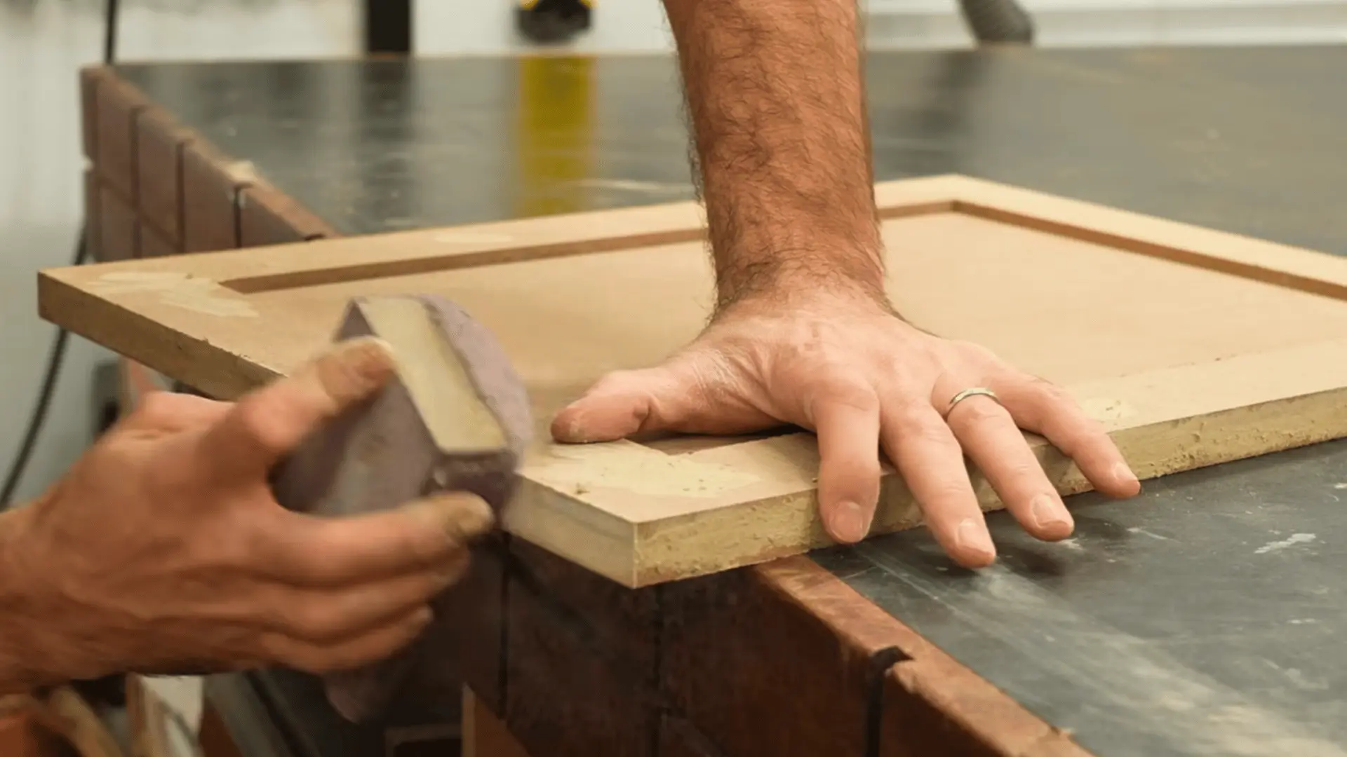 woodworker sanding the edge of an MDF cabinet door with a sanding block before priming and painting