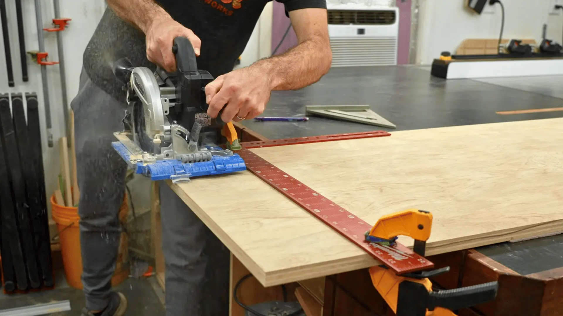 woodworker using a circular saw with an edge guide clamped to plywood to make a straight rip cut