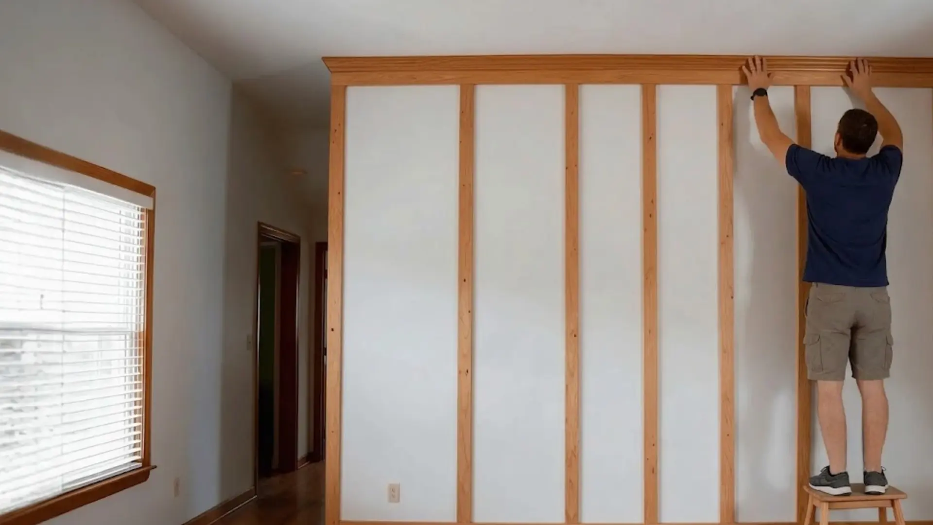 person hammering the top trim piece above evenly spaced battens on a board and batten wall
