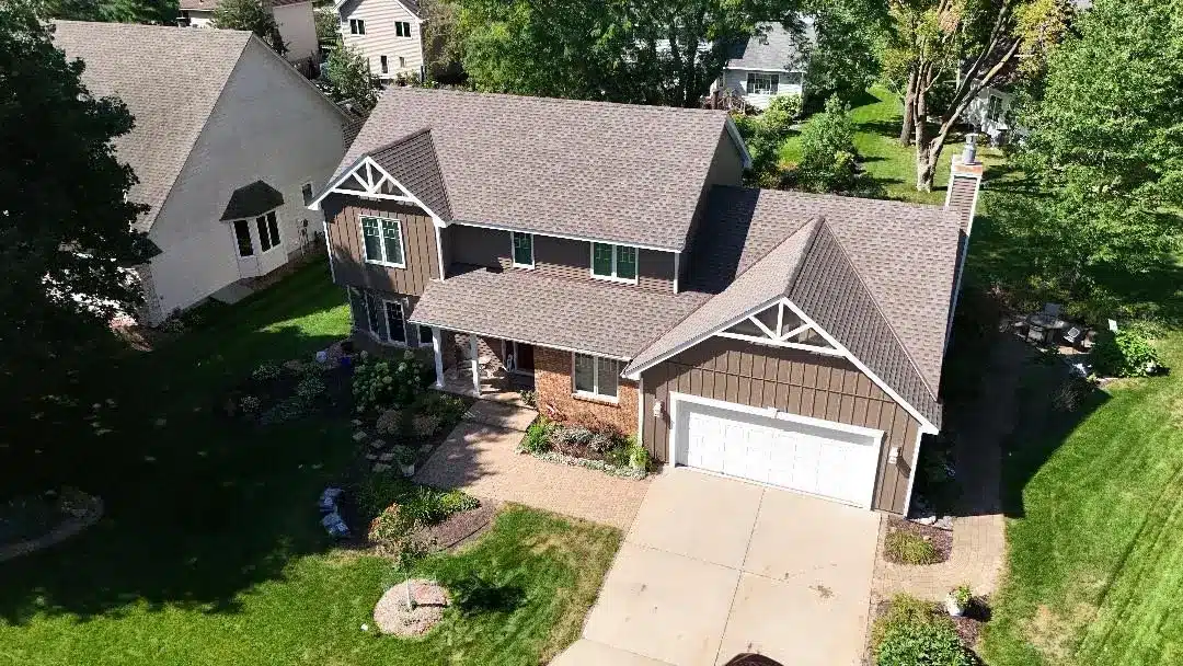 Aerial view of a two-story suburban house with brown siding and manicured lawn