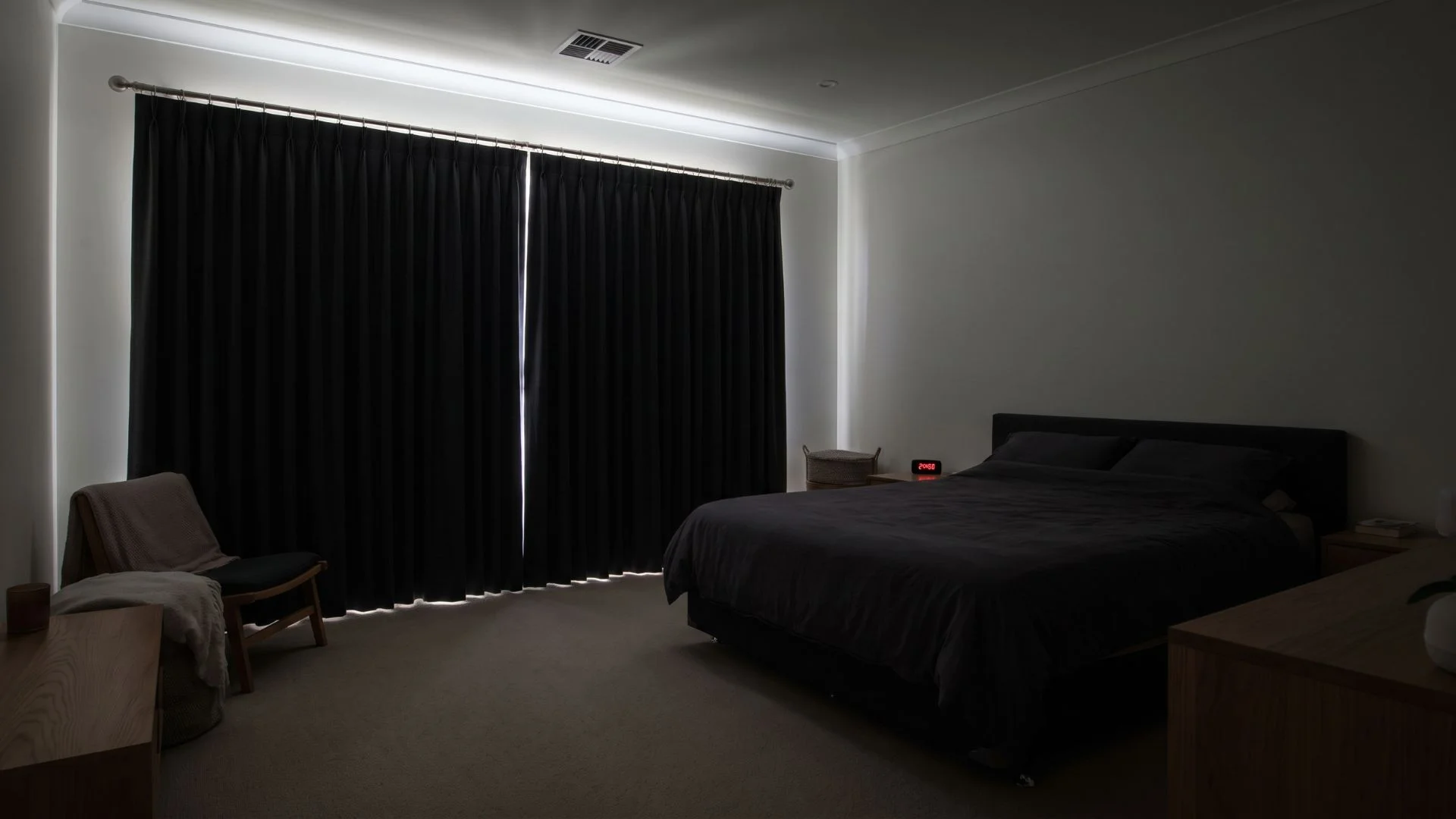 dark bedroom with black blackout curtains covering a wide window beside a neatly made bed