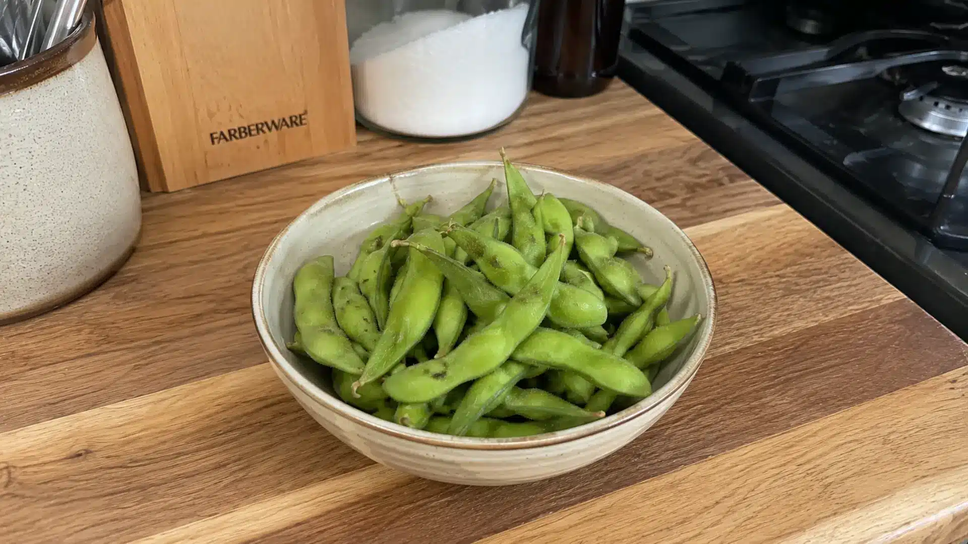 fresh green edamame pods in a ceramic bowl on a wooden kitchen counter