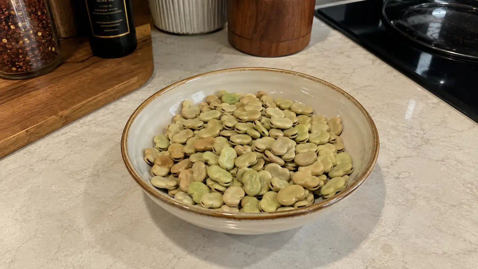dry large flat fava beans (broad beans) in kitchen a bowl, on a white marble counter
