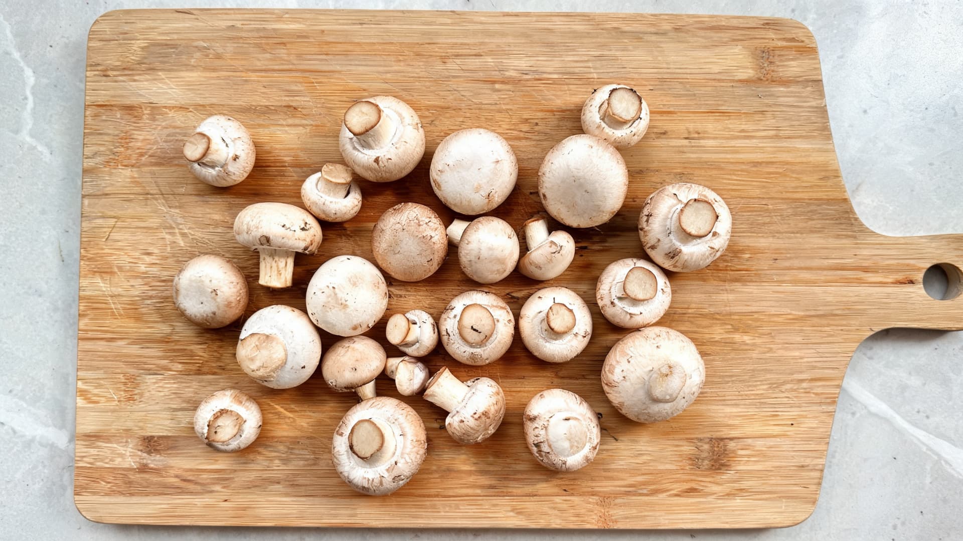 fresh whole white button mushrooms scattered on wooden cutting board with handle