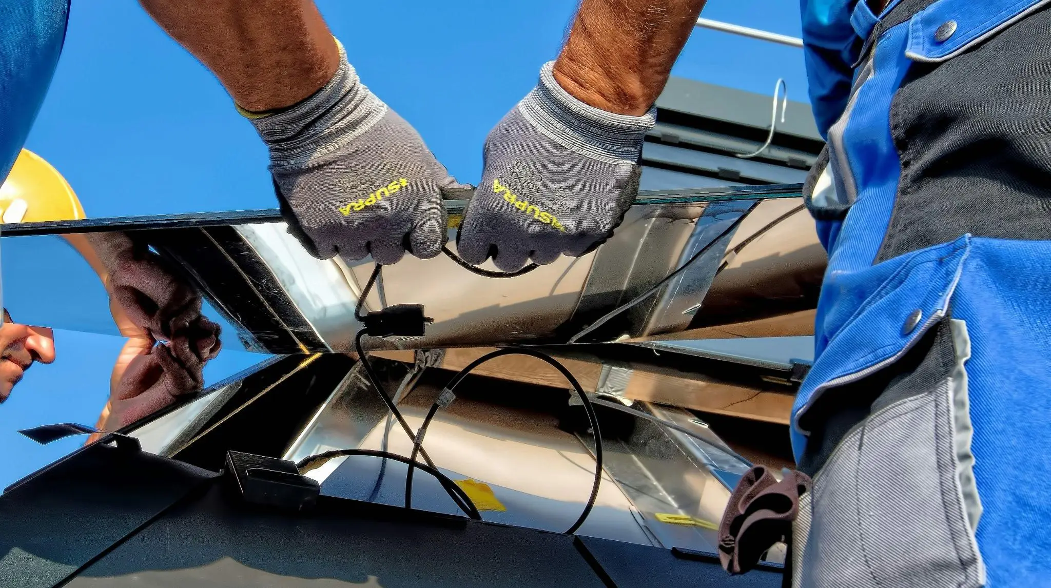 Worker installing solar panels on a rooftop under clear blue sky