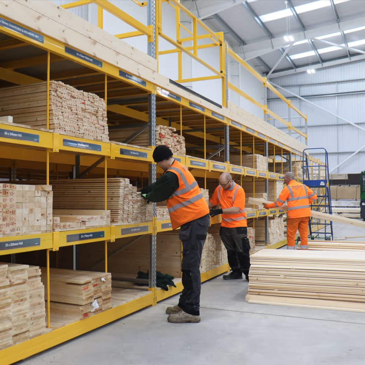 Workers organizing wooden planks on industrial shelves in large warehouse with high ceiling