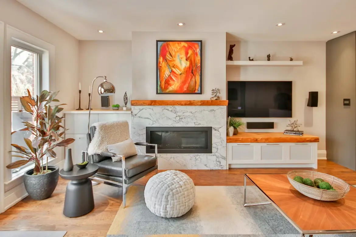 Modern living room with marble fireplace, abstract art, and cozy seating area featuring greenery