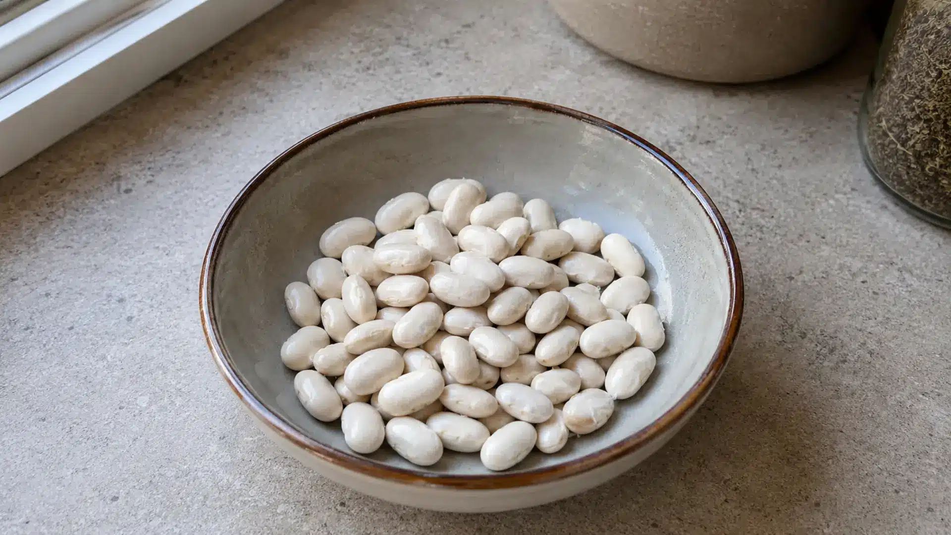 small white navy beans in a small ceramic bowl on a kitchen counter