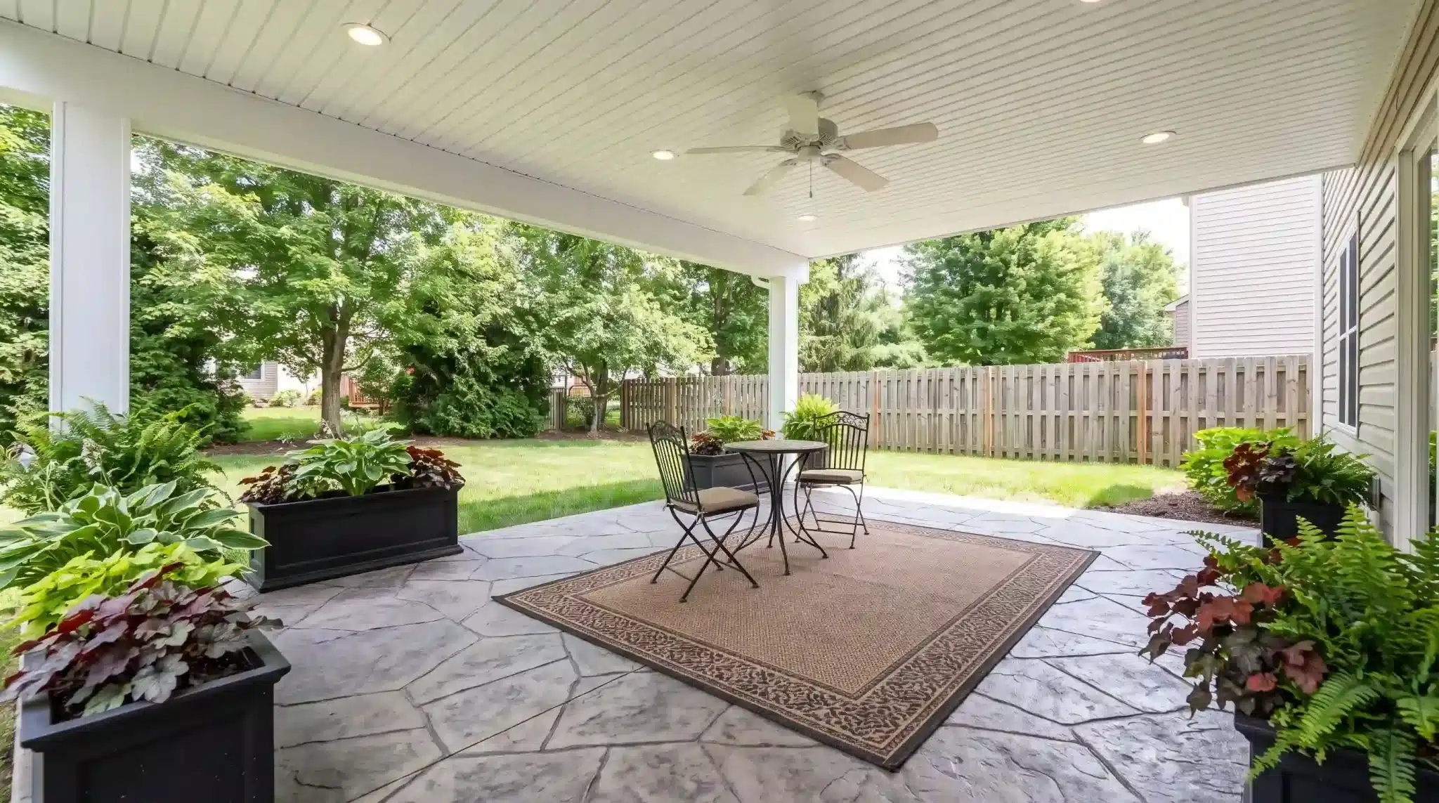 covered outdoor patio with a dining table, ceiling fan, potted plants, and a fenced backyard