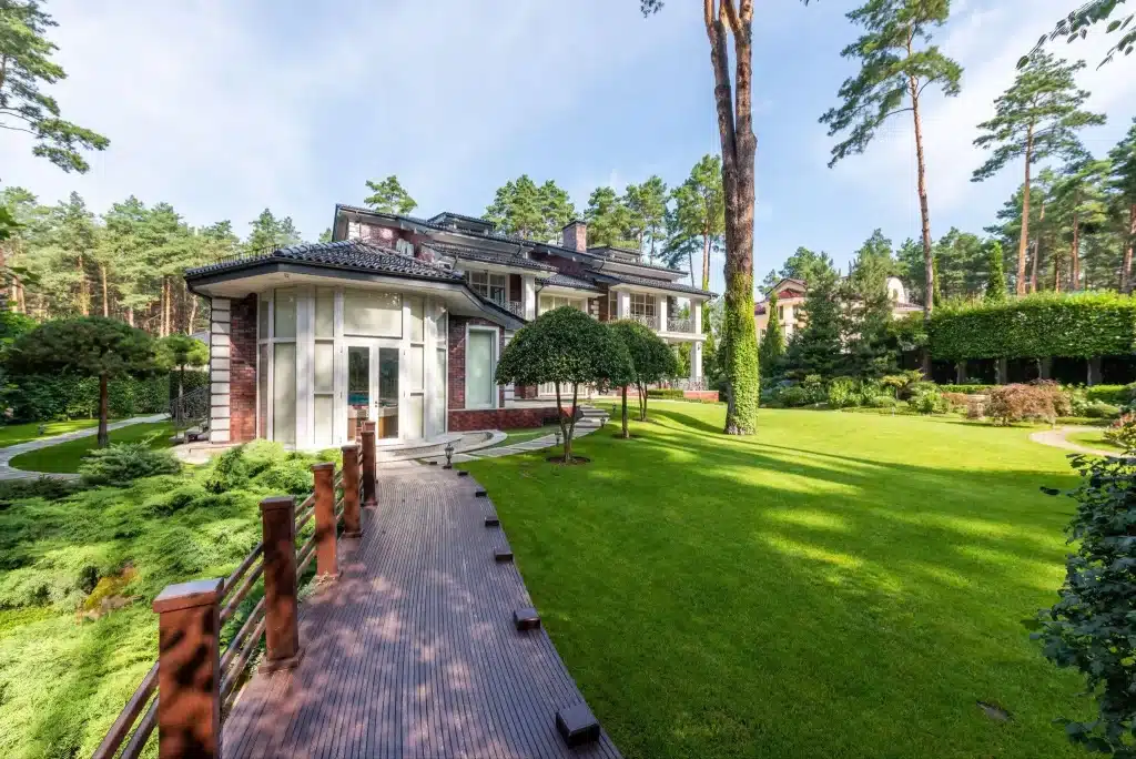 Large modern house with lush green lawn and tall pine trees in a sunny garden setting
