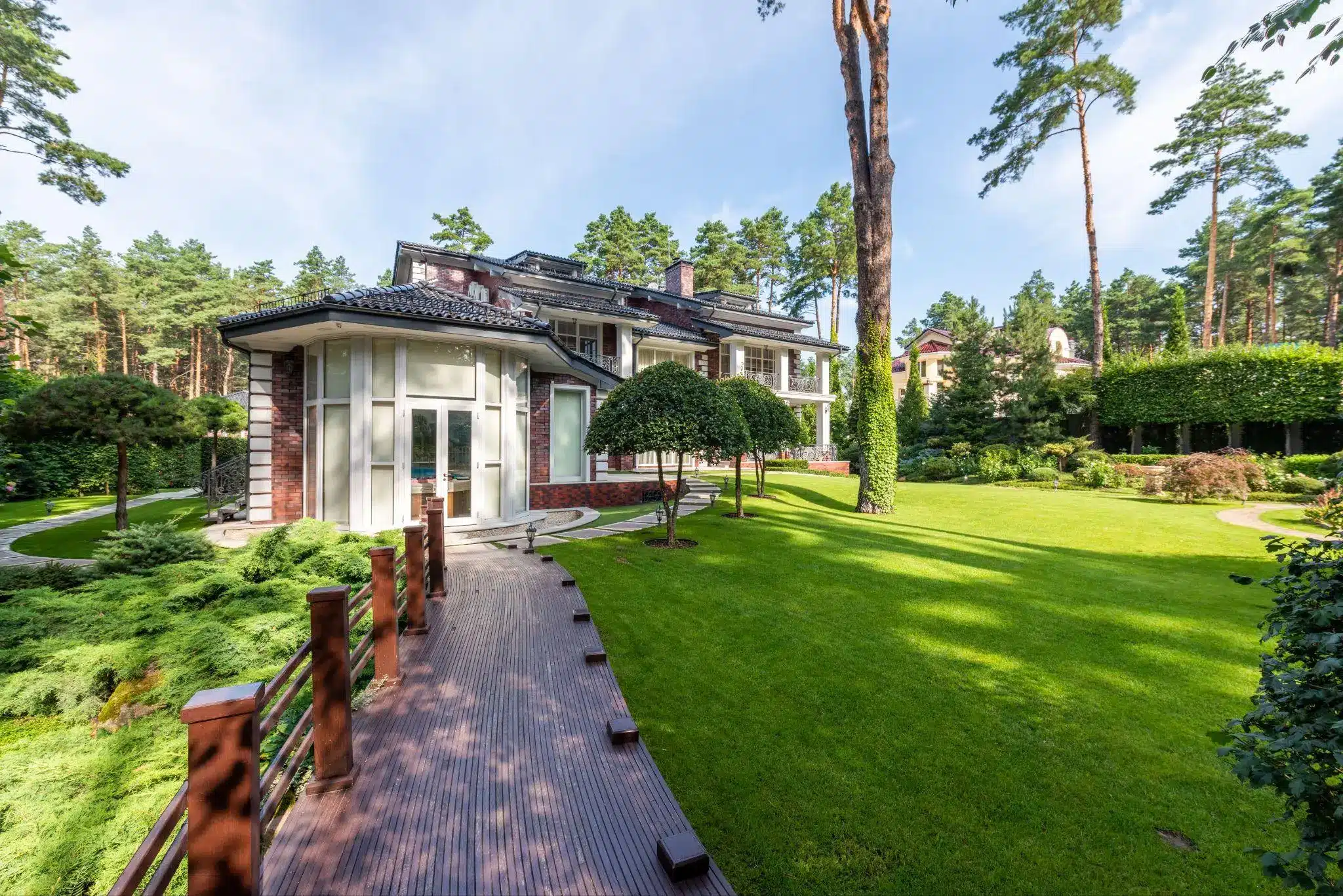 Large modern house with lush green lawn and tall pine trees in a sunny garden setting