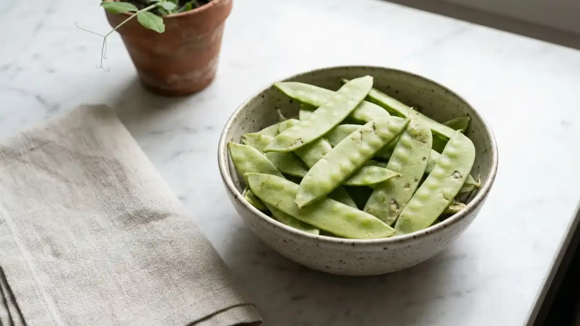 snow peas in a bowl showing their flat pale green pods with visible seed outlines