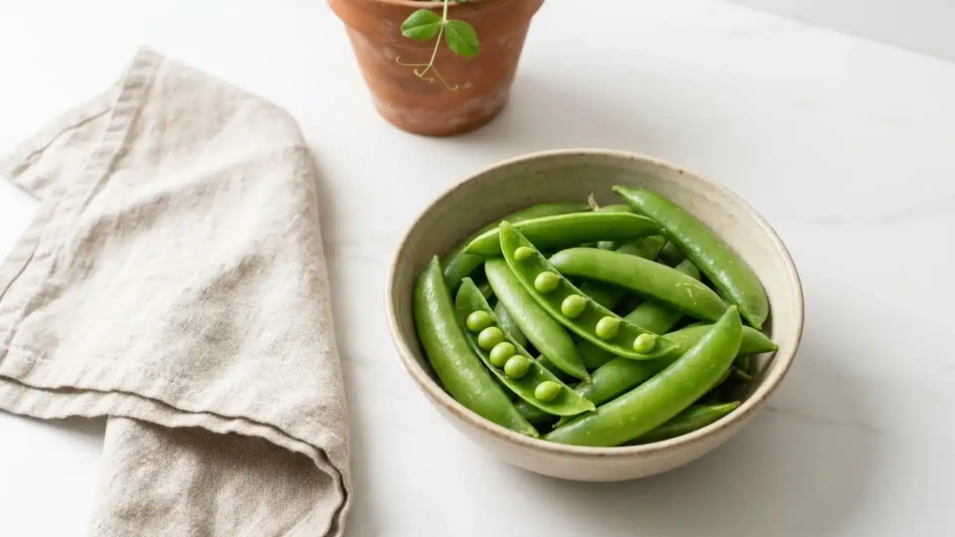 fresh sugar snap peas in a bowl with a couple of pods split open showing plump peas inside