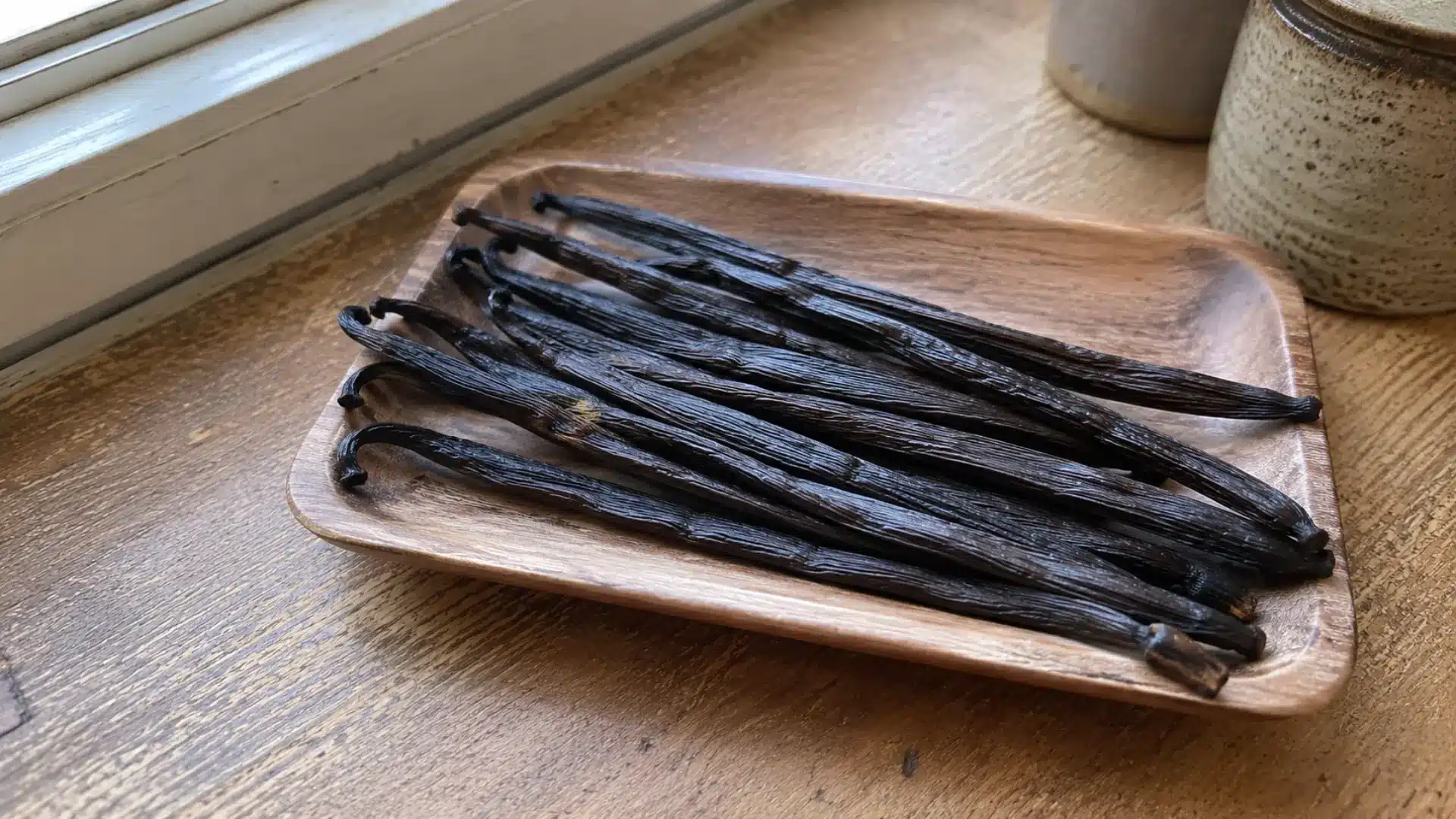 whole dark vanilla bean pods on a small wooden tray