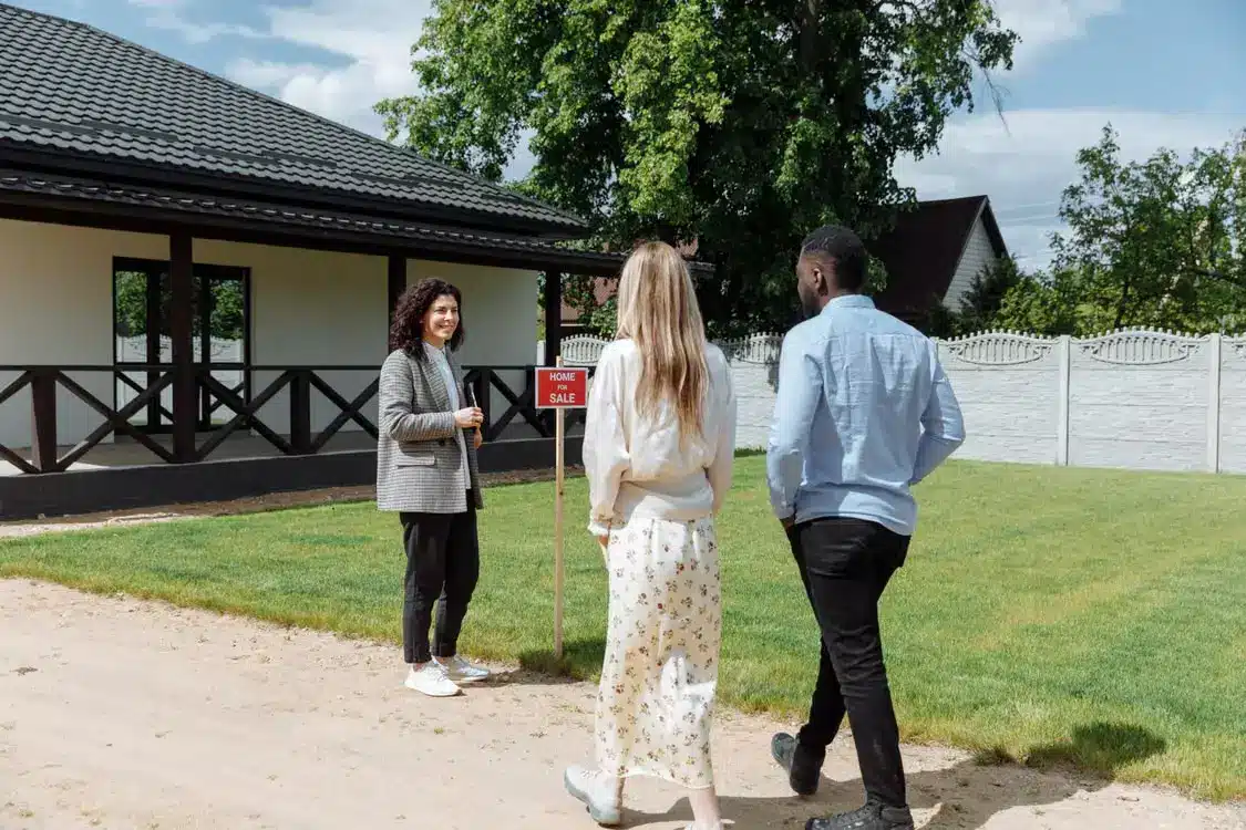 Real estate agent showing a house for sale to a couple outside in sunny weather