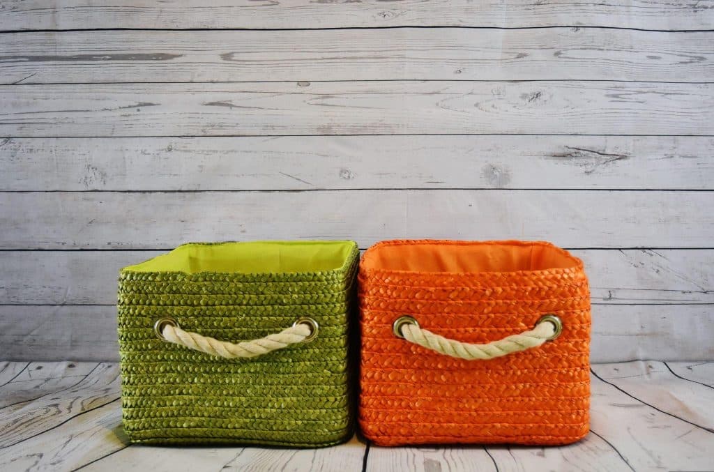 Green and orange woven storage baskets with rope handles on wooden floor background