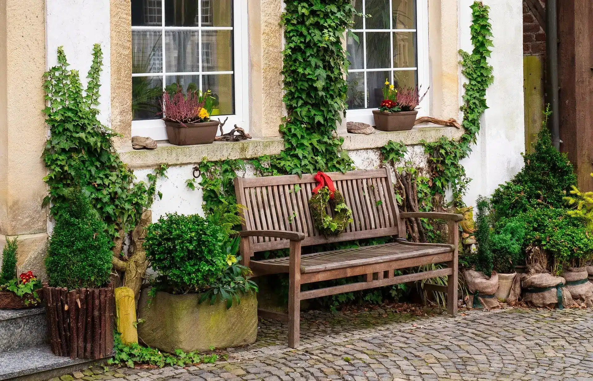 Wooden bench with wreath in ivy-covered garden setting near large windows